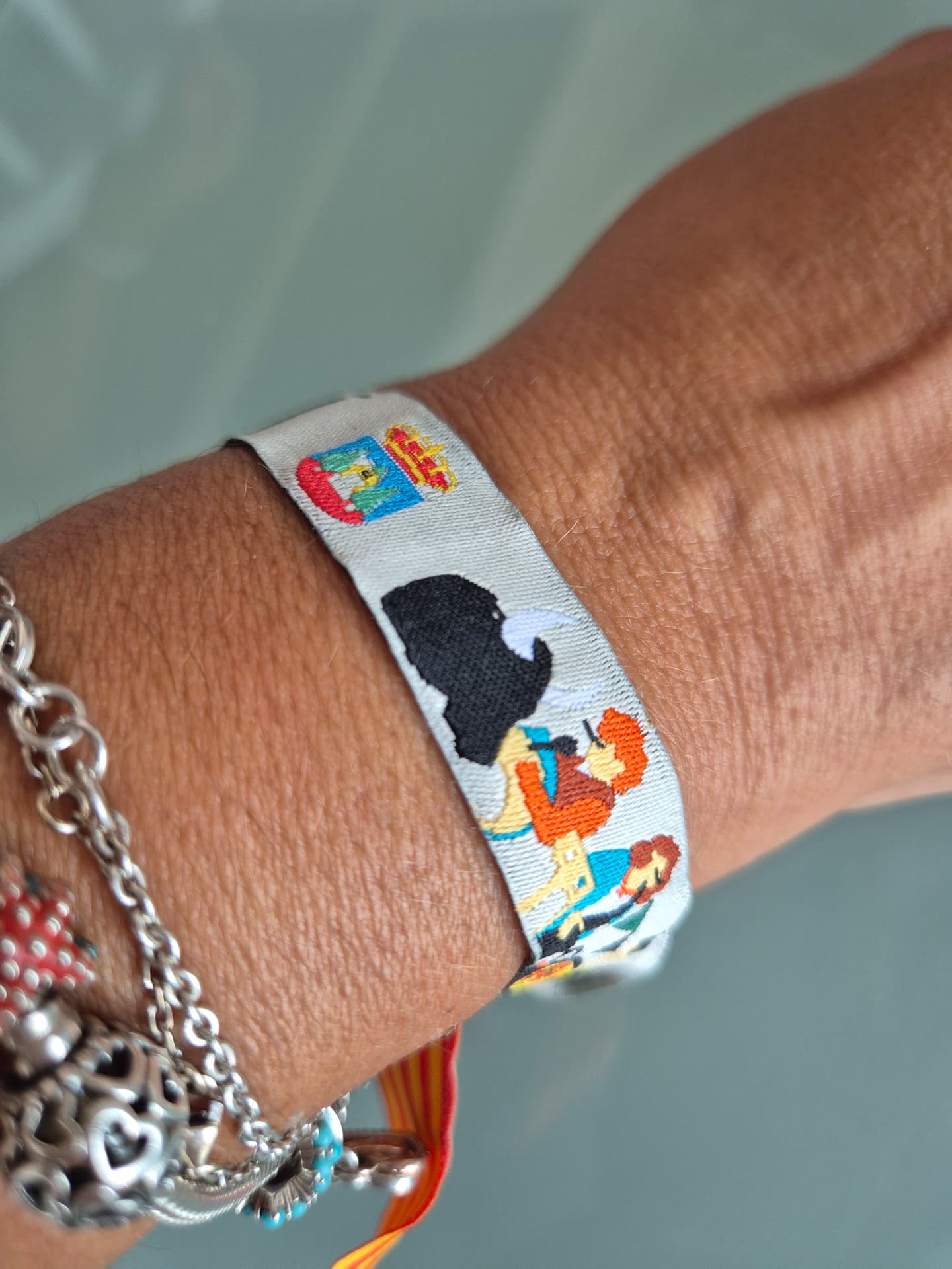 Pulsera de tela personalizada en blanco con escudo municipal y figuras festivas, puesta en la muñeca