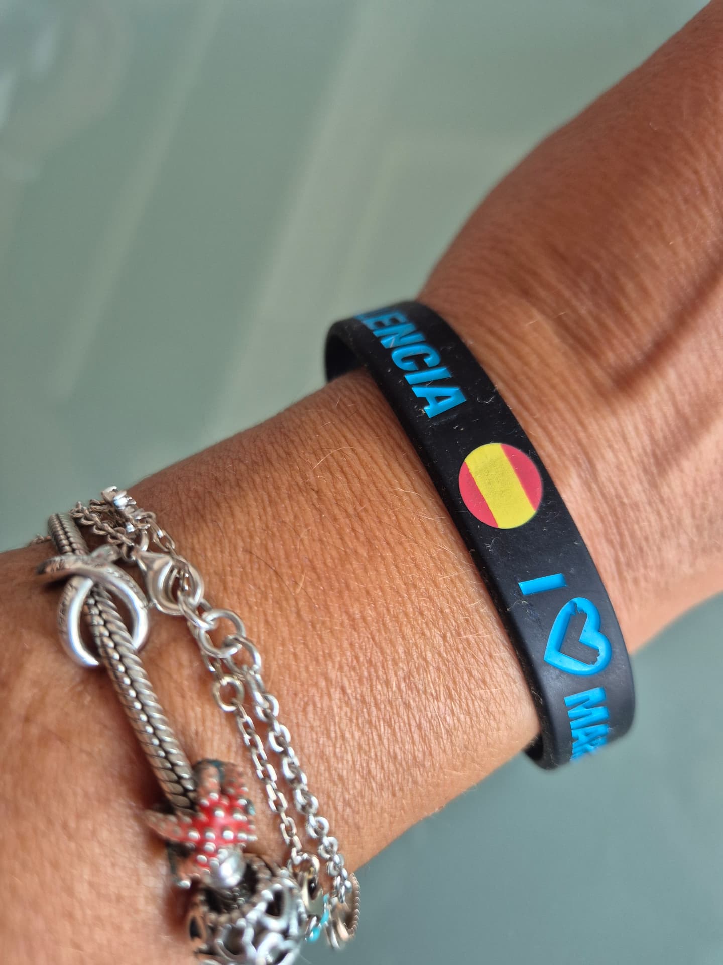 Pulsera de silicona negra con inscripciones en azul y bandera de España, puesta en la muñeca